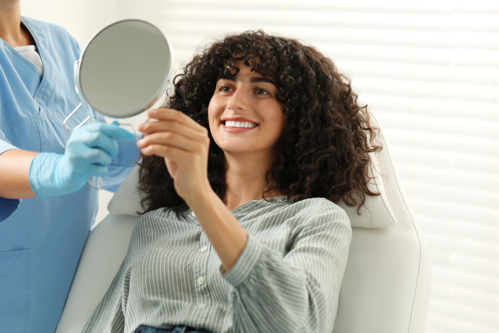 A SmilePro Dental patient looking at her new smile in a hand mirror after treatment