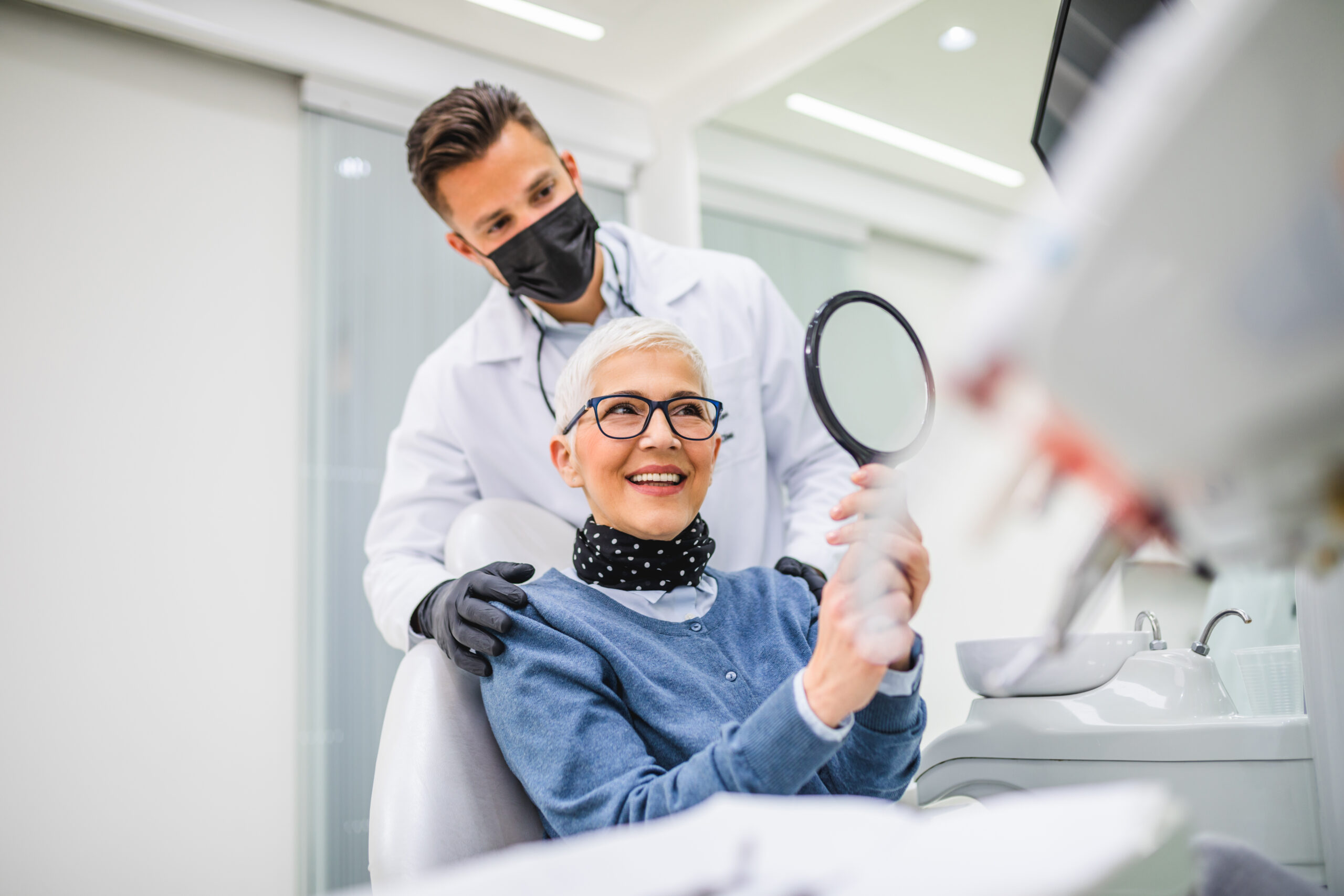 Beautiful senior woman having dental treatment at dentist's office. Dentist is wearing protective face mask due to coronavirus pandemic.