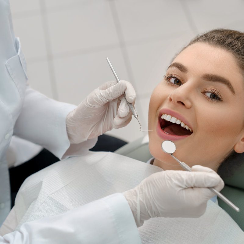 View from above of young woman lying on dental chair with open mouth and looking at camera while professional doctor checking teeth. Concept of dentistry procedure and stomatology.View from above of young woman lying on dental chair with open mouth and looking at camera while professional doctor checking teeth. Concept of dentistry procedure and stomatology.View from above of young woman lying on dental chair with open mouth and looking at camera while professional doctor checking teeth. Concept of dentistry procedure and stomatology.